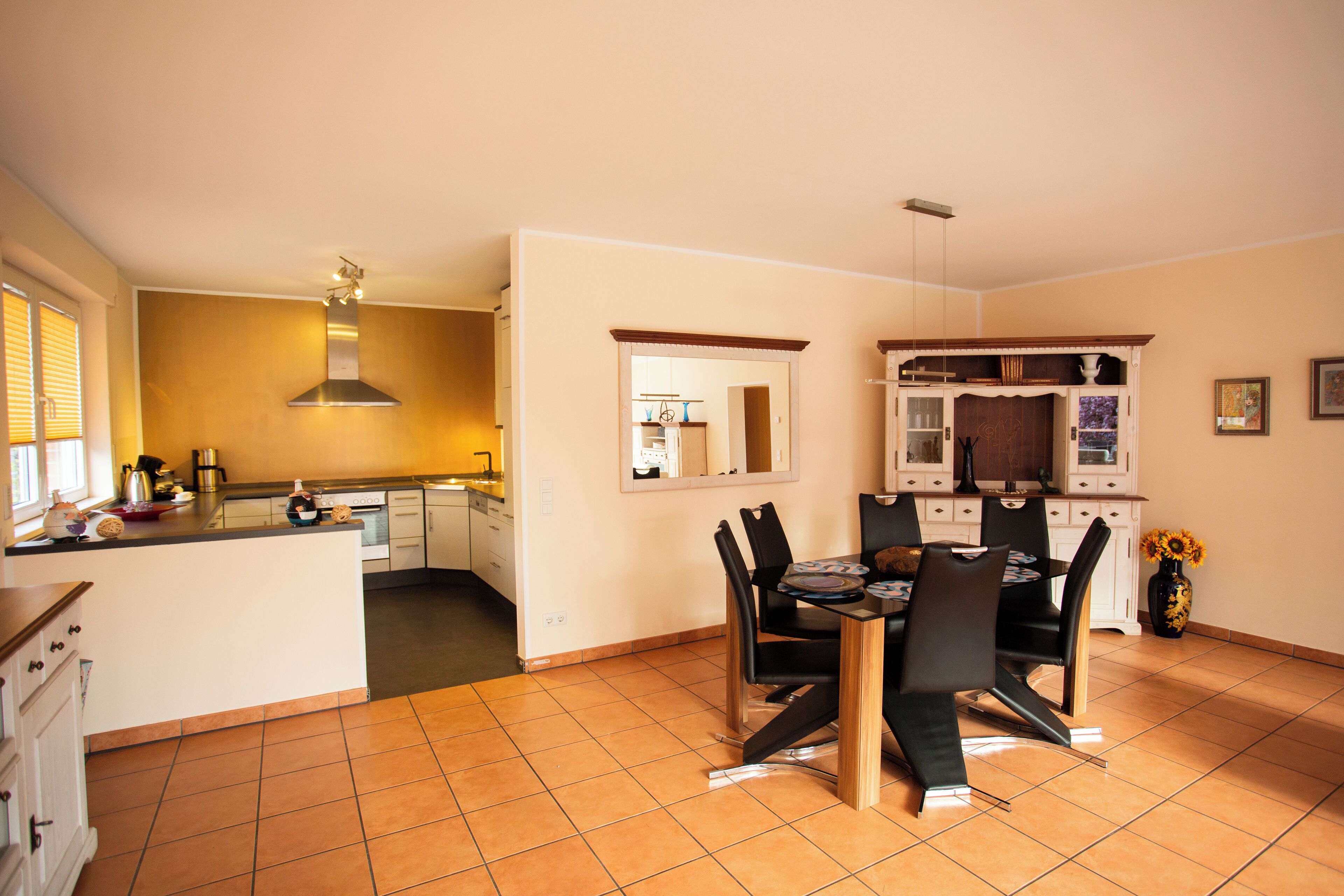 A spacious kitchen with a central island, a dining area with a table and chairs, and a large mirror above the island.