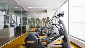 Un gimnasio con varias máquinas de cardio, un muro de cristal y vistas a la ciudad.