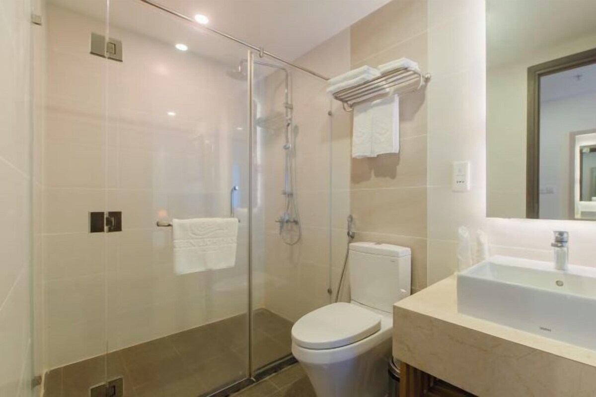 Un baño moderno con ducha de vidrio, inodoro blanco y lavamanos con espejo superior.