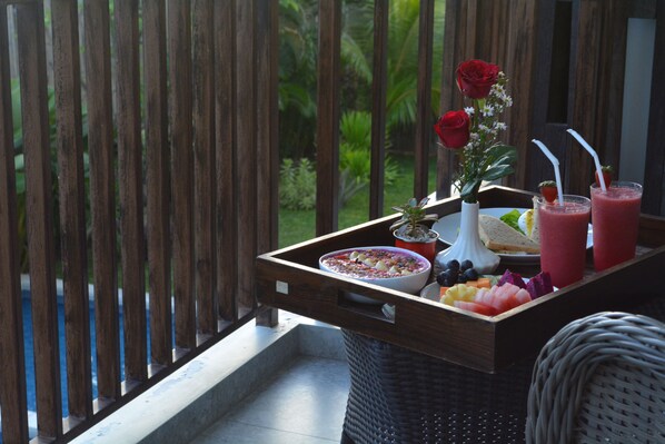 A wooden balcony with a tray of food and drinks, a vase with flowers, and a view of greenery. - Tevana (Keroboken Kelod)