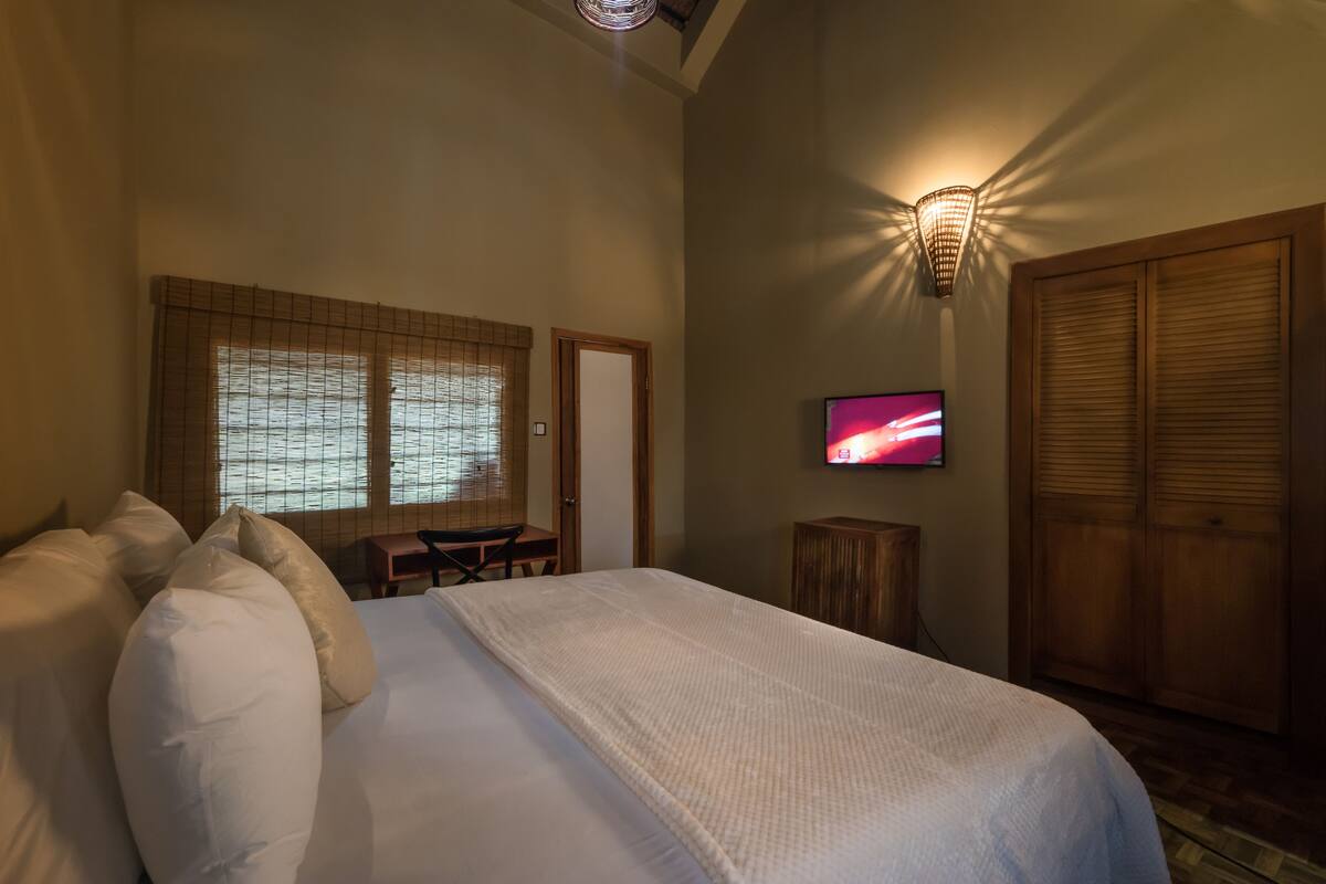 A hotel room with a large bed, a television, a desk, and a wardrobe.