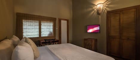 Ein Hotelzimmer mit einem großen Bett, einem Fernseher, einem Schreibtisch und einem Kleiderschrank.