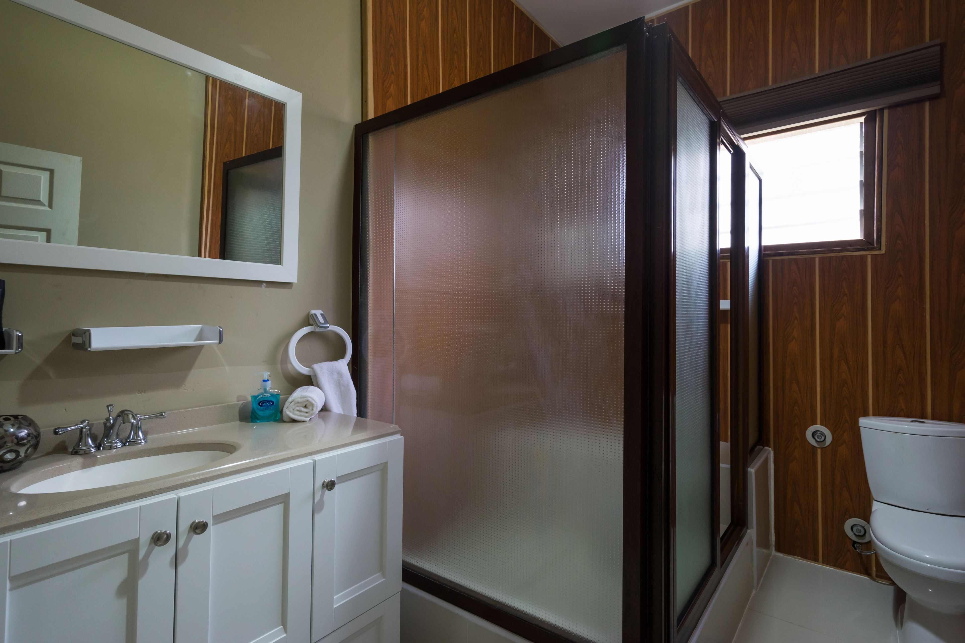 A bathroom with a white sink, mirror, and toilet. There is a shower enclosure with a frosted glass door.