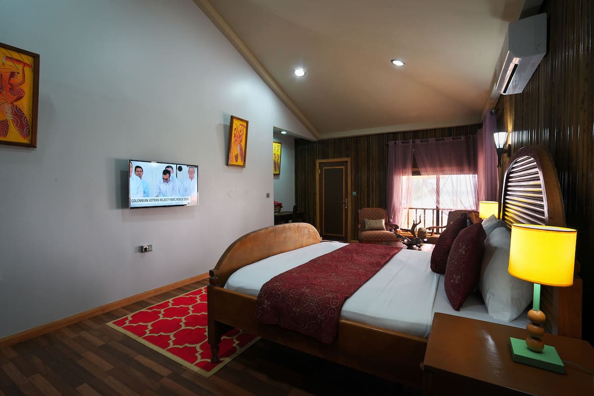 A hotel room with a bed, a television, a lamp, and a red rug.