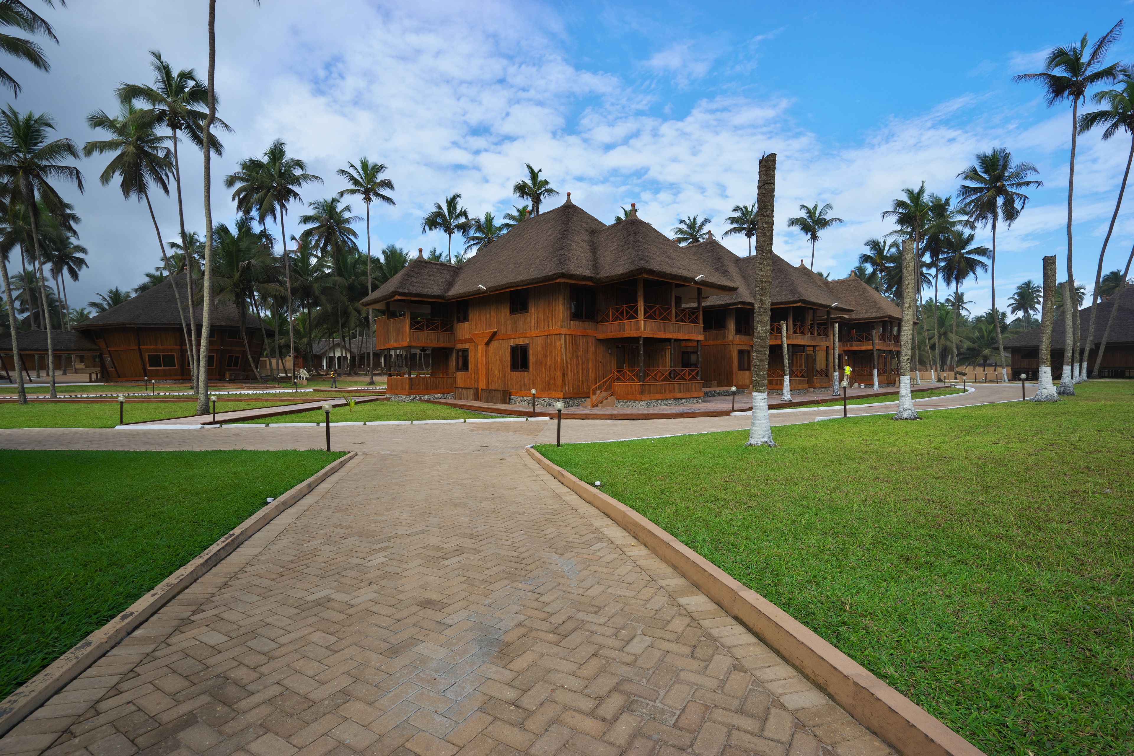 Un resort con edificios de madera, palmeras y un sendero pavimentado.