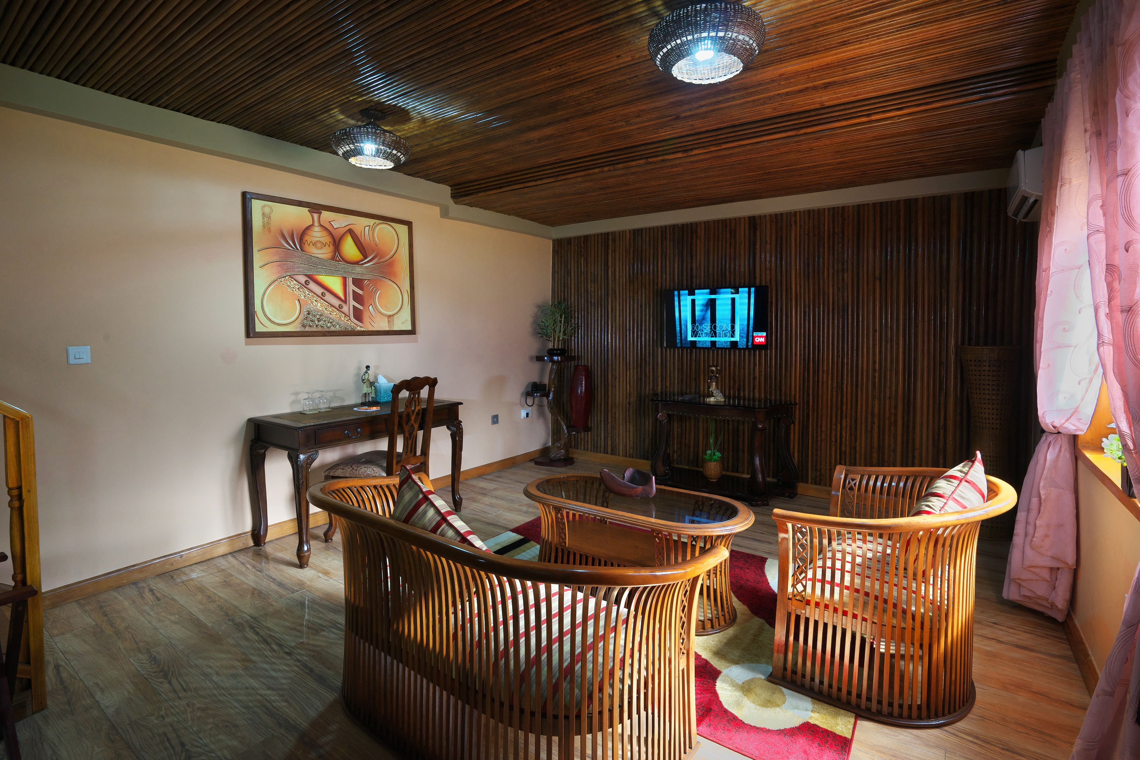 Una sala de estar con techo de madera, televisor, mobiliario de mimbre y un cuadro en la pared.