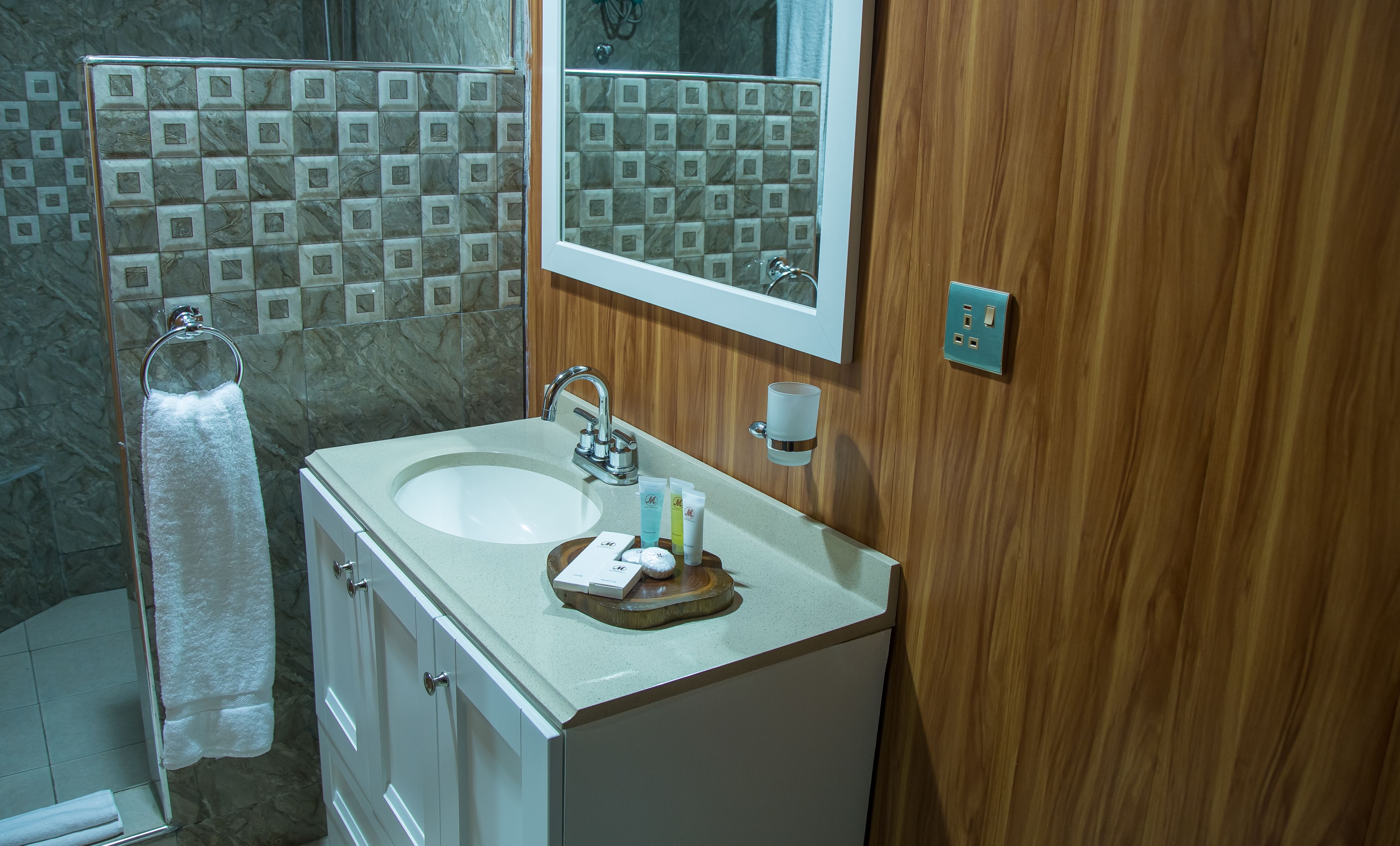 Un baño con ducha de azulejos de mármol, un lavabo con artículos de aseo y un tocador de madera.