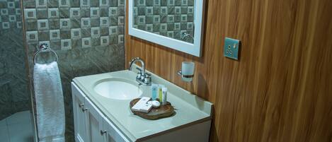 Un baño con ducha de azulejos de mármol, un lavabo con artículos de aseo y un tocador de madera.