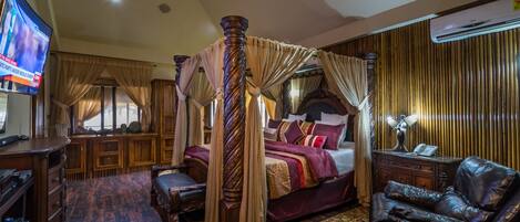 A luxurious bedroom with a four-poster bed, a leather armchair, a television, and a decorative rug.