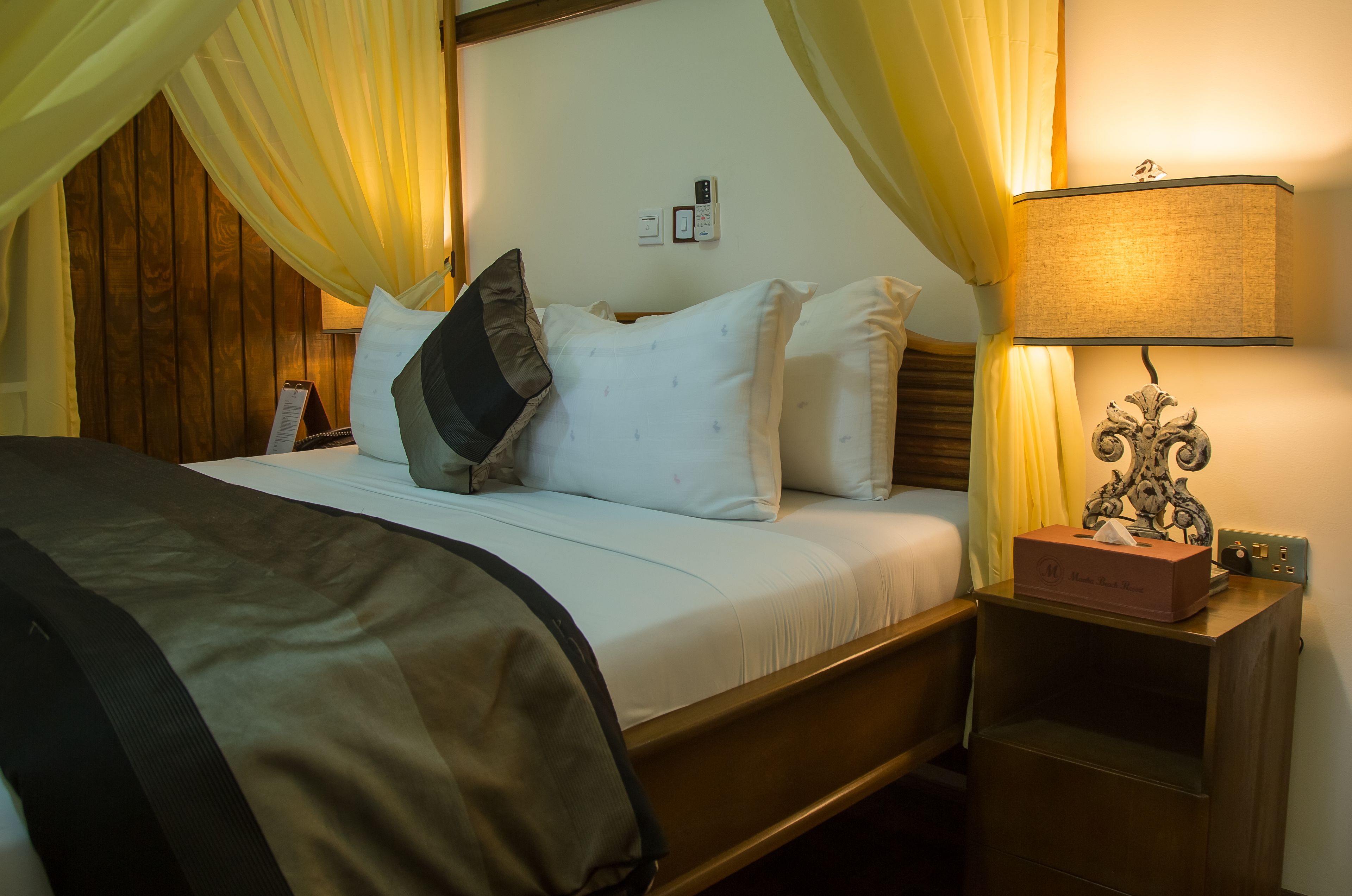 A hotel room with a bed, a nightstand, a lamp, and a box on the nightstand.