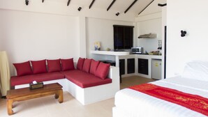 A modern room with a sectional sofa, a wooden coffee table, a bed with a red bedspread, and a kitchenette area. - Karo Villas (Koh Tao)