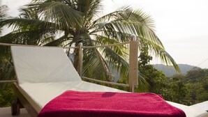 A single bed with a white mattress and a red towel, positioned on a balcony with a view of palm trees and a mountainous landscape. - Karo Villas (Koh Tao)