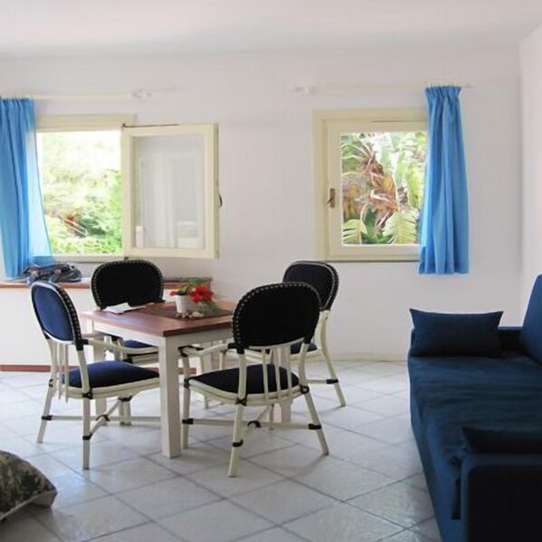 Una habitación con una mesa de comedor y sillas, un sofá y dos ventanas con cortinas.
