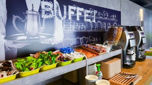 A buffet area with a variety of food items, including fruits, vegetables, and prepared dishes. There are multiple coffee machines and a large poster on the wall advertising the buffet. - ibis budget Toulouse Colomiers (Colomiers)