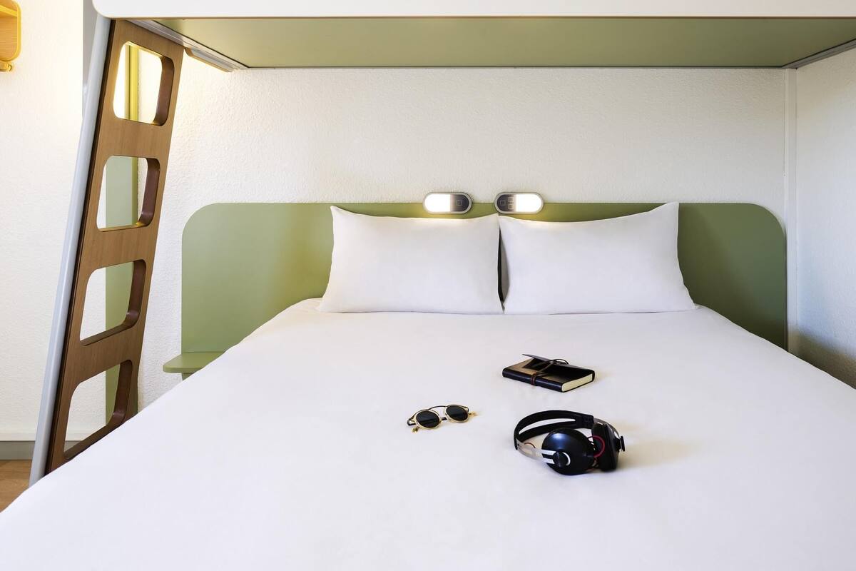 Una cama bien hecha con ropa de cama blanca, dos almohadas, unas gafas de sol y un auricular sobre la cama.