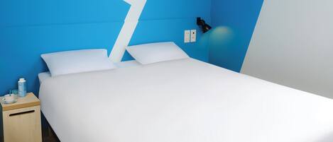 Una habitación de hotel moderna con una cama, una mesita de noche, una lámpara y una pared azul decorativa.