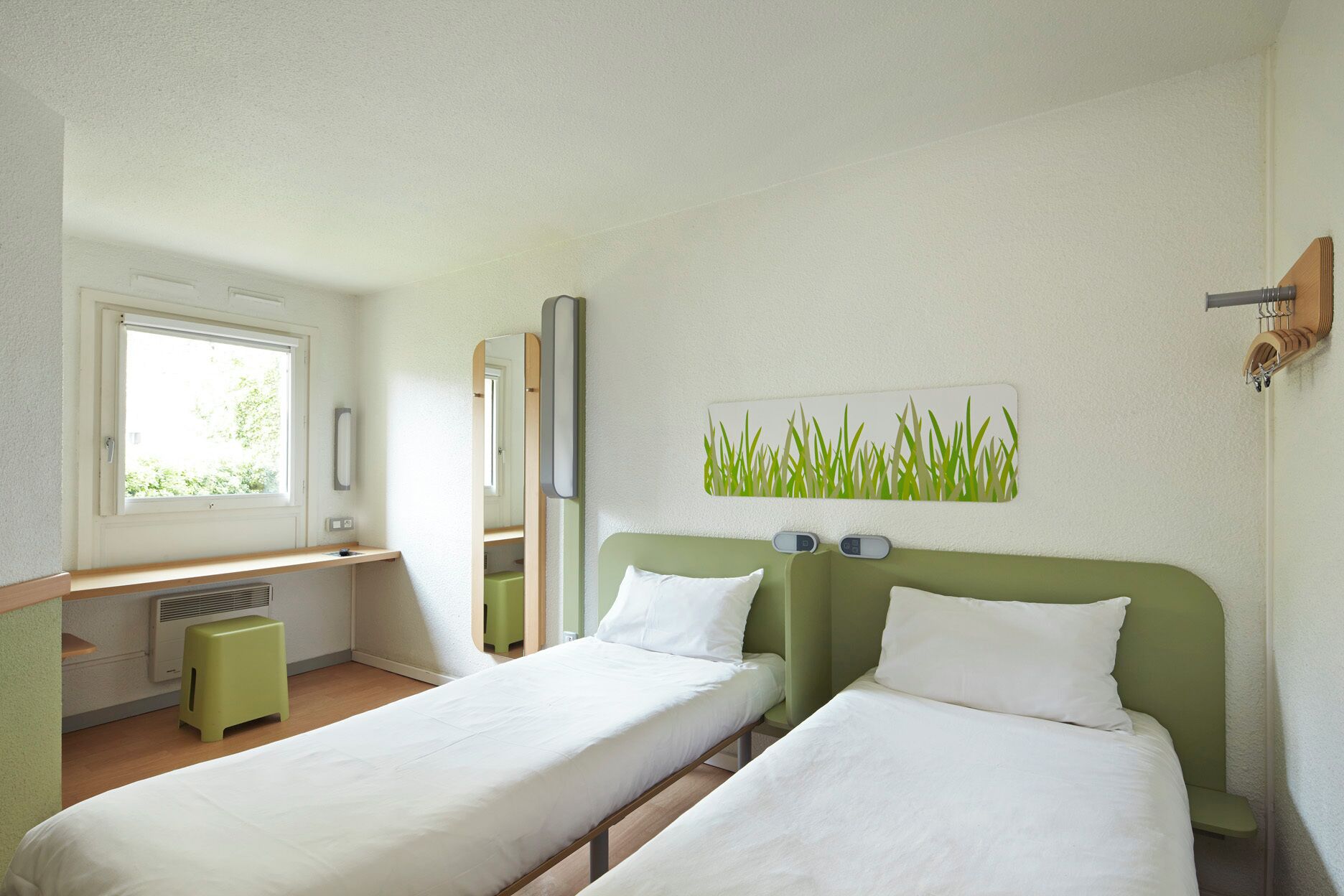 A room with two single beds, a small desk, a mirror, and a window.