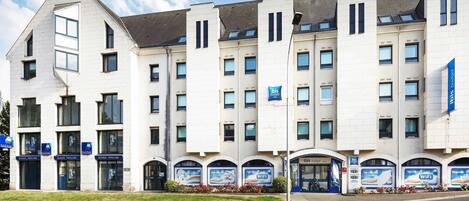 Un edificio de varios pisos con una entrada destacada, un letrero que dice 'ibis budget' y varias ventanas.