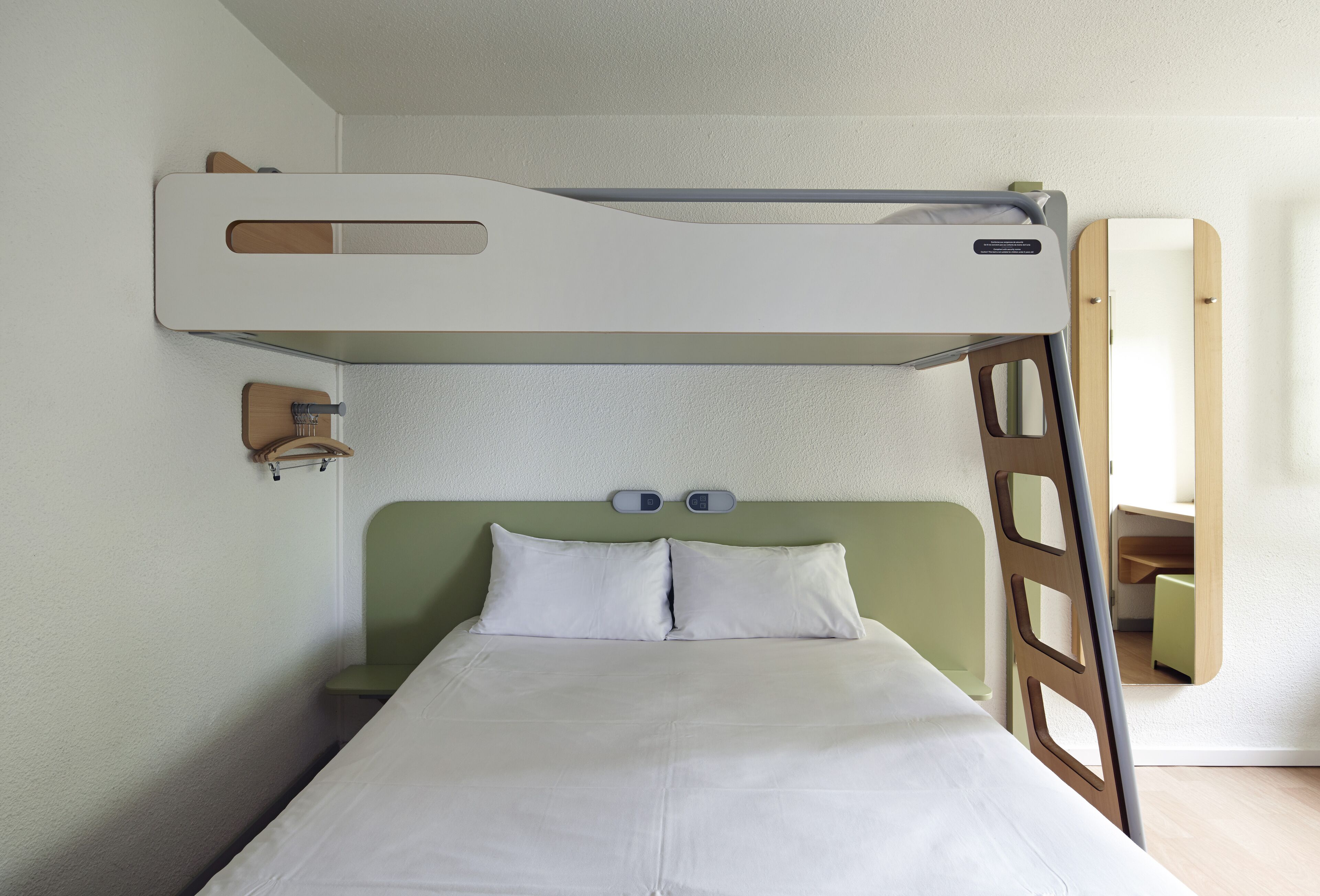 A bunk bed with a ladder, a bedside table, and a mirror on the wall.