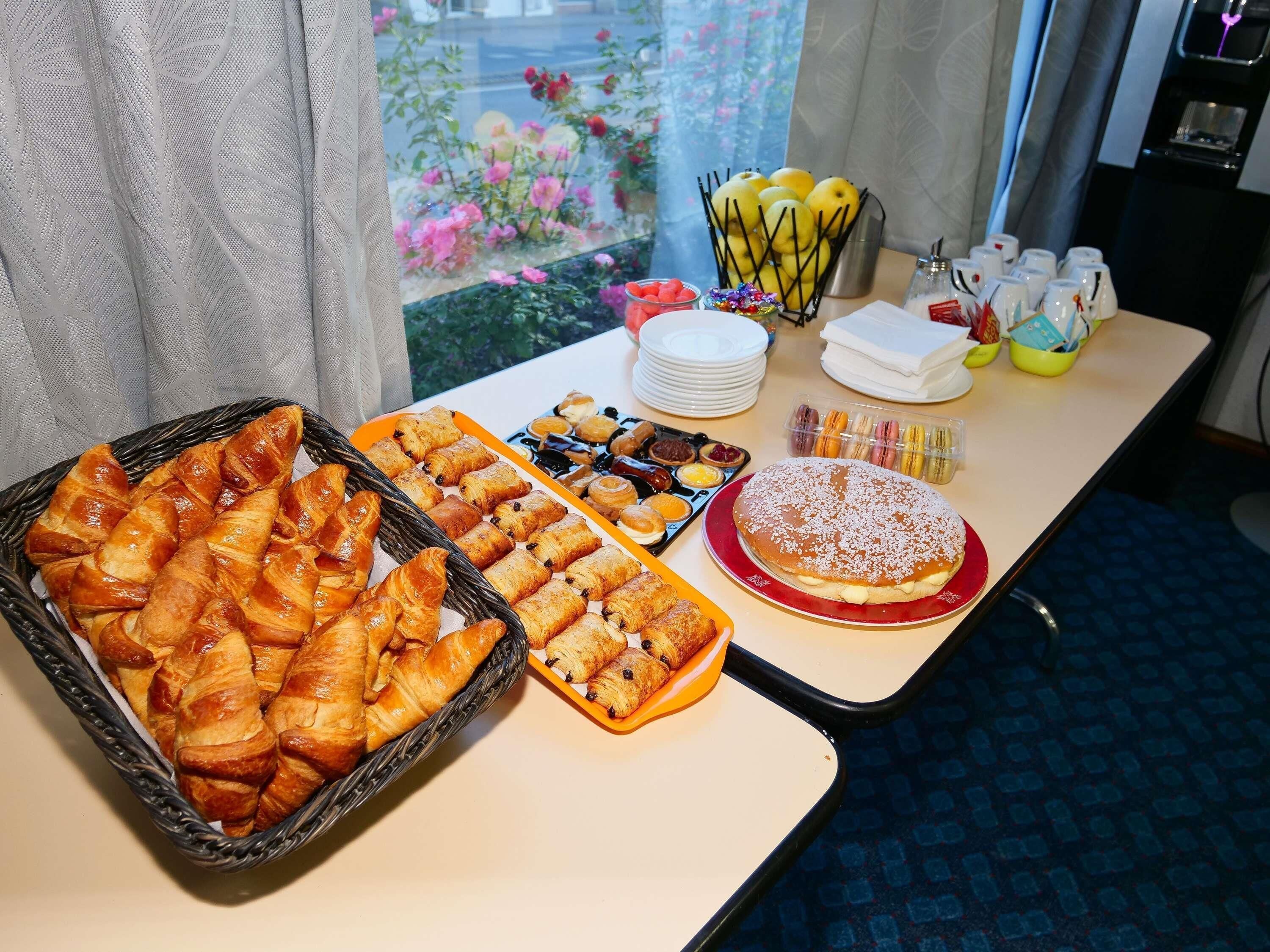 Une table de buffet avec divers pâtisseries, un panier de fruits et un distributeur d’eau.