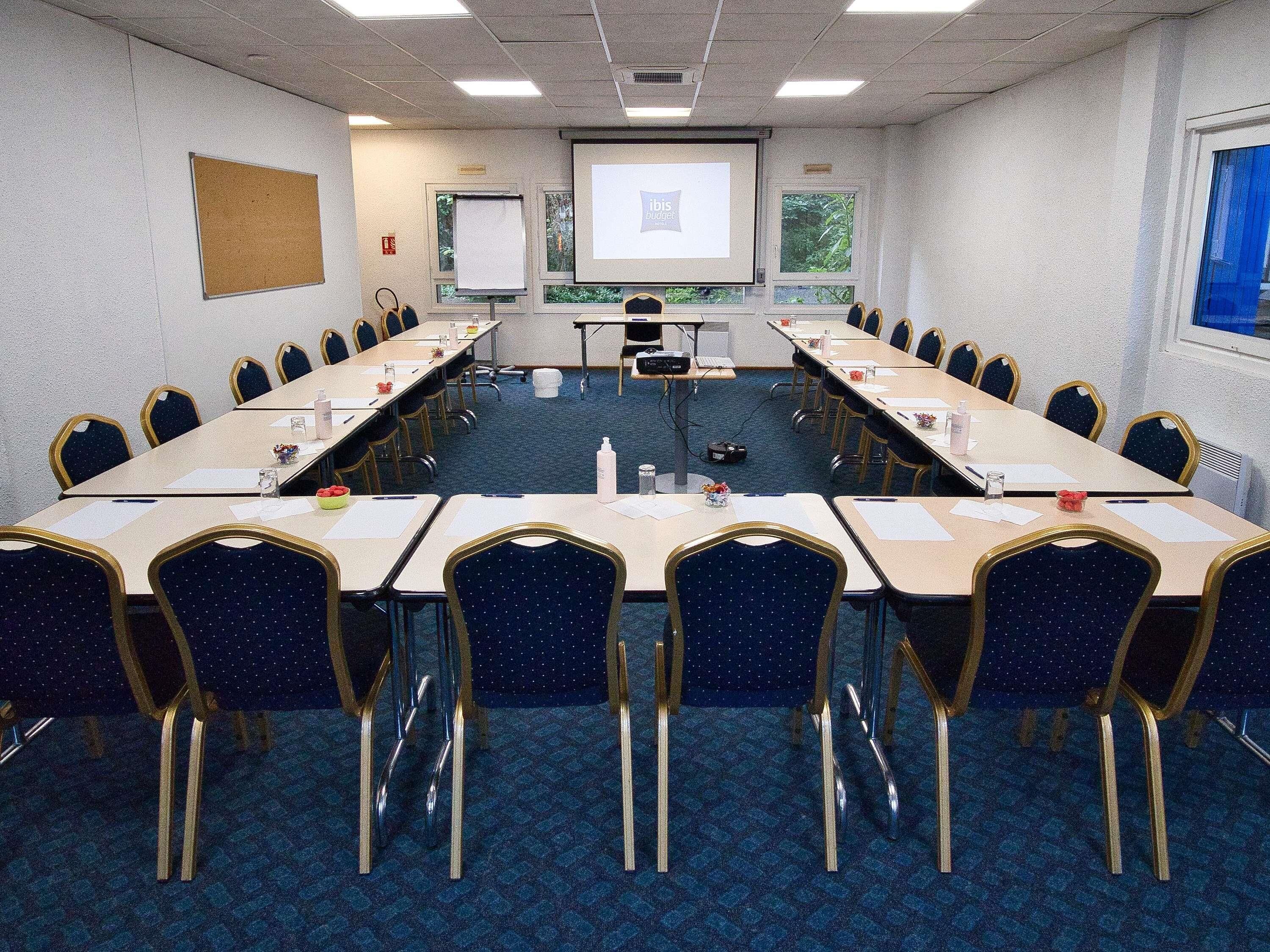 Une salle de conférence équipée d’une longue table, de chaises, d’un écran de projection et d’un écran de présentation.