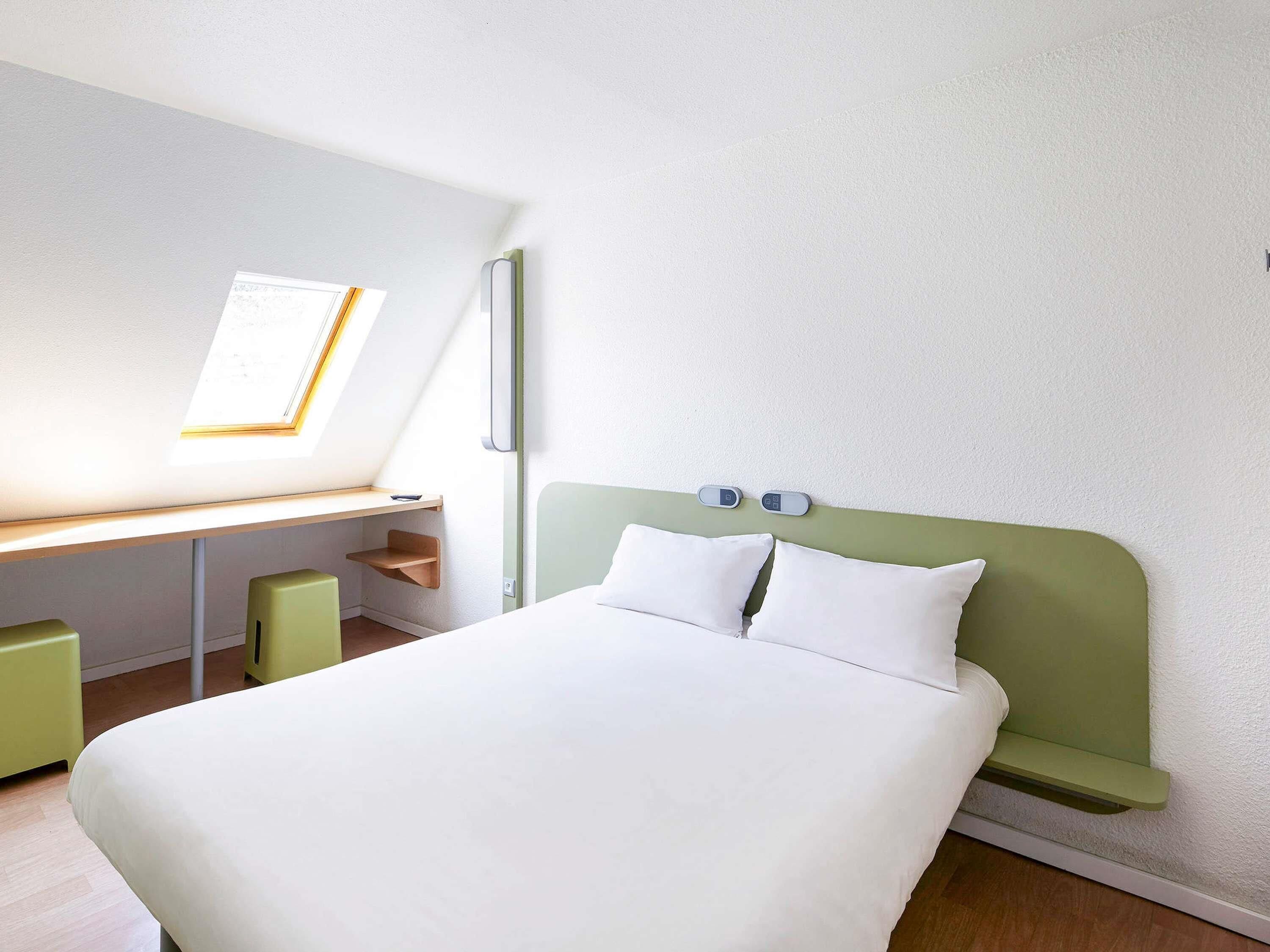 A bedroom with a bed, a desk, and a window.