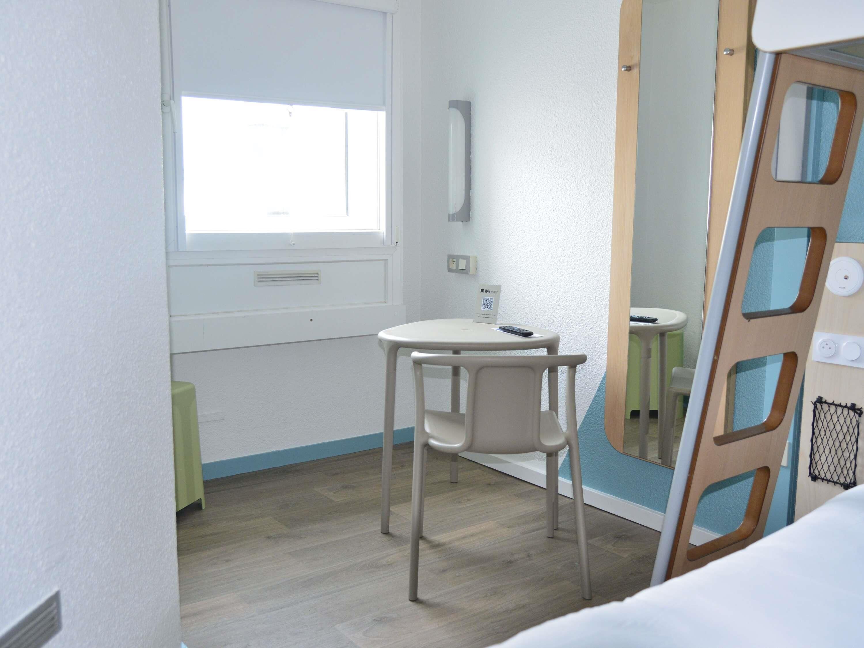 A small, well-lit room with a single white chair, a small table, and a window.