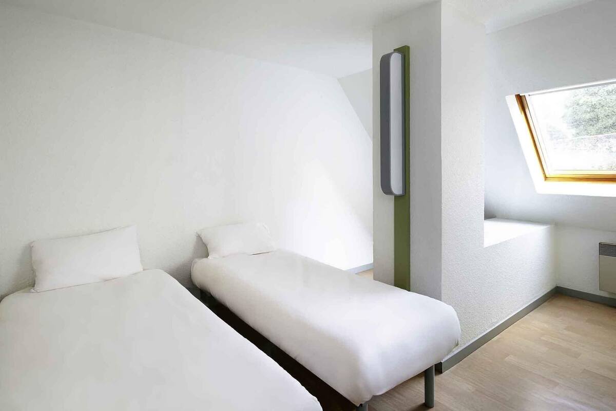 Une chambre moderne avec deux lits, une fenêtre et un luminaire fixé au mur.