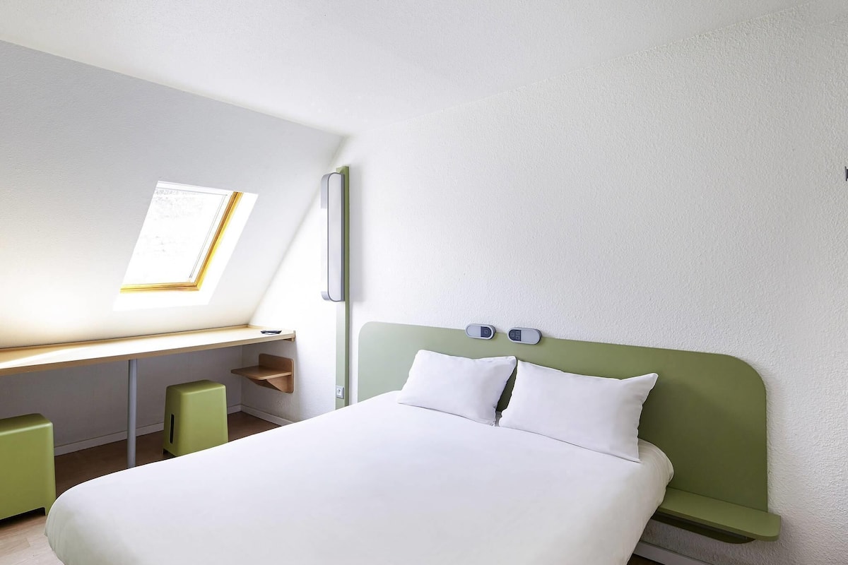 Quarto de hotel com cama, escrivaninha e janela.