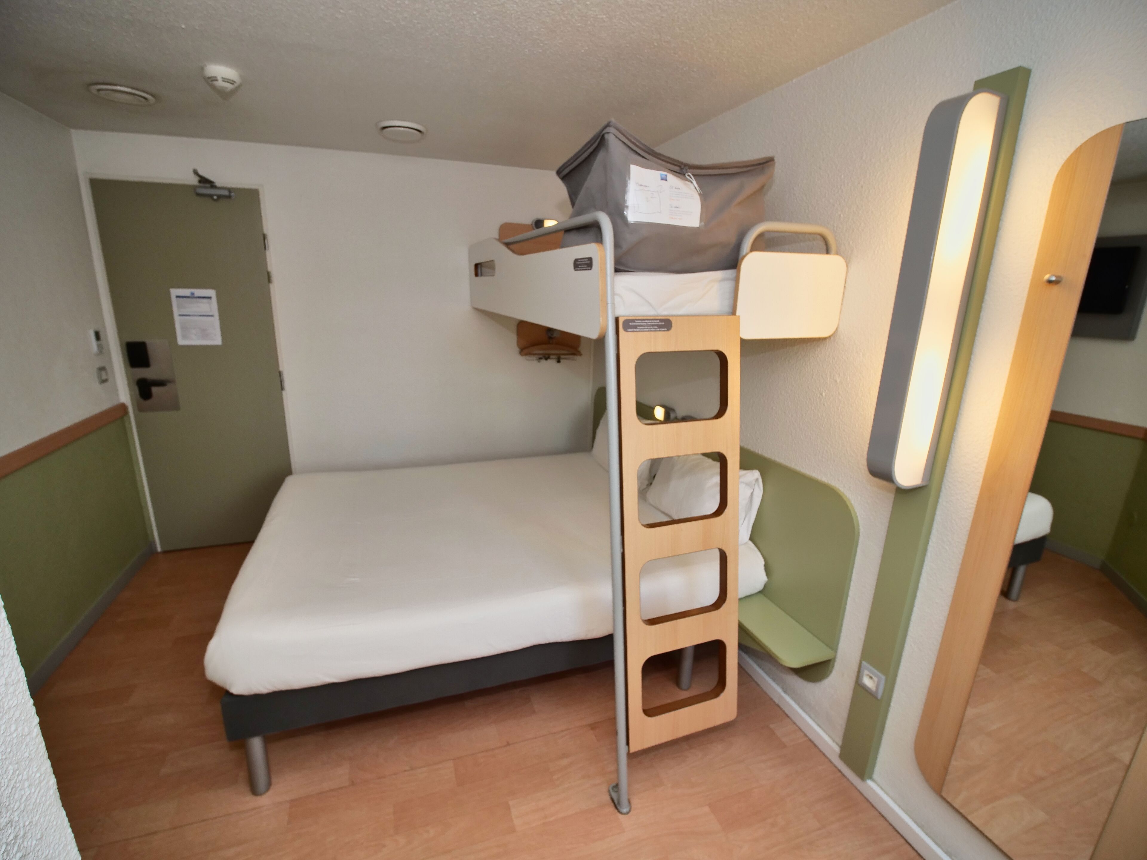 A bunk bed with a ladder, a small bedside table, and a mirror.