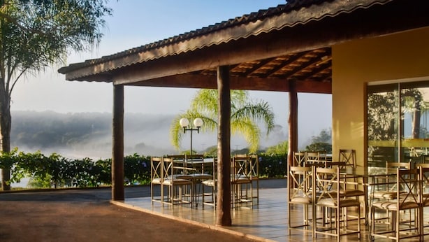 Una terrazza esterna con tavoli e sedie, una zona coperta con pavimento in piastrelle e vista su un paesaggio montuoso.