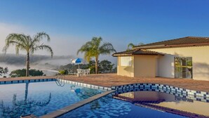 Una piscina con bordi piastrellati, un piccolo edificio con tetto in tegole e palme.