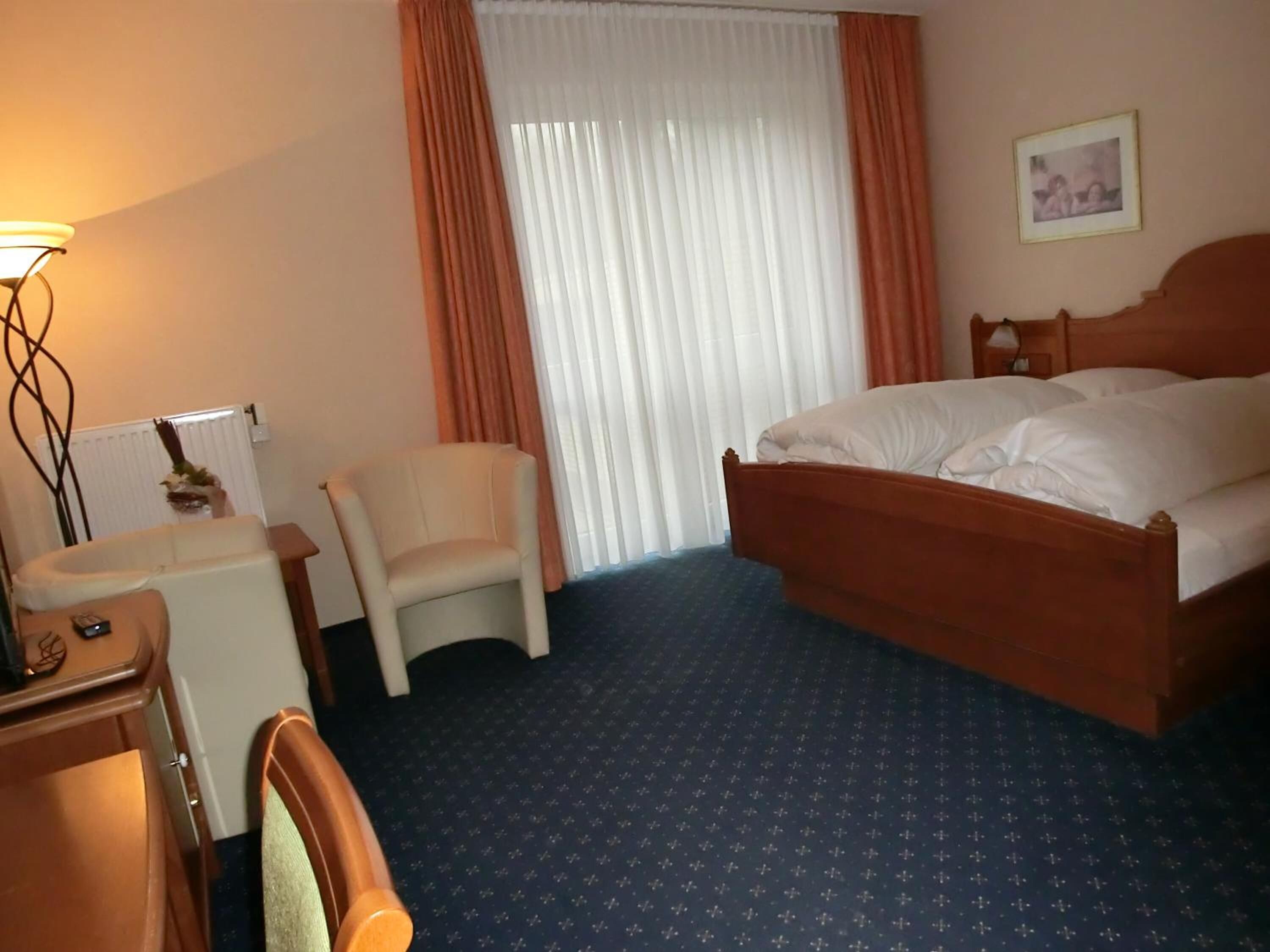 A hotel room with a bed, a chair, a desk, and a lamp.