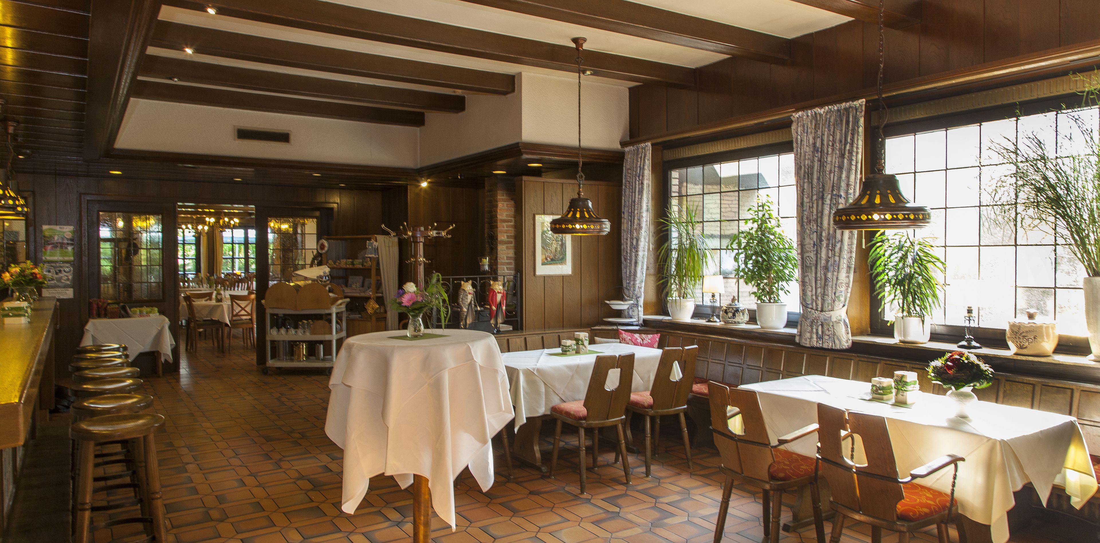 Un restaurant au décor intérieur en bois, avec des nappes blanches et des plantes en pot.