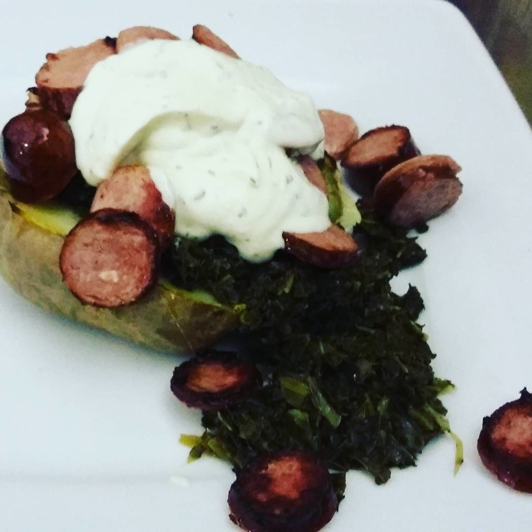 A plate with a baked potato topped with sausage slices and a dollop of white sauce.
