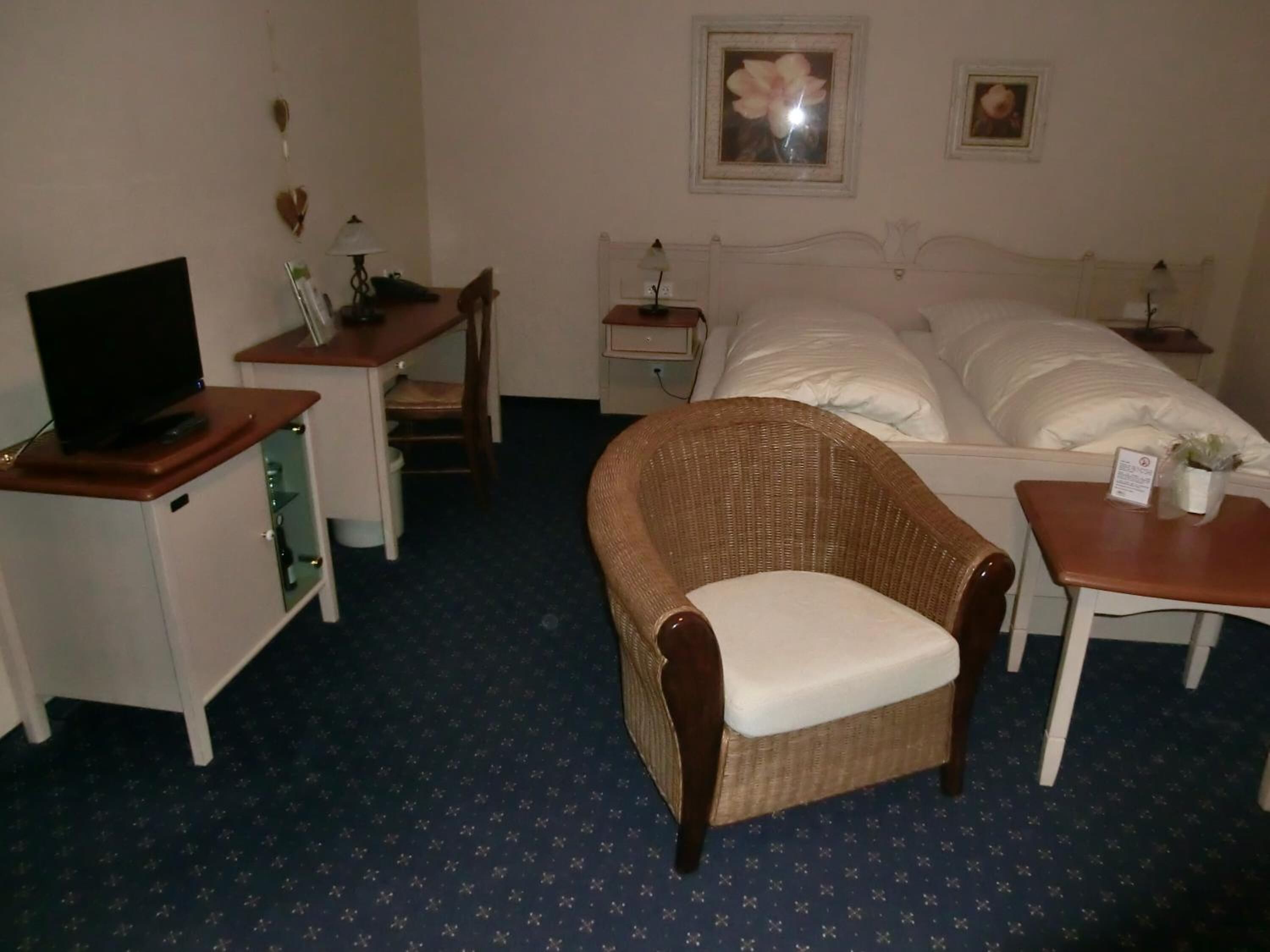 A hotel room with a bed, a television on a cabinet, a wicker chair, and a small table with a plant.