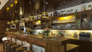 Un espace bar doté de tabourets en bois, de luminaires suspendus et d’étagères remplies de bouteilles et de verres.