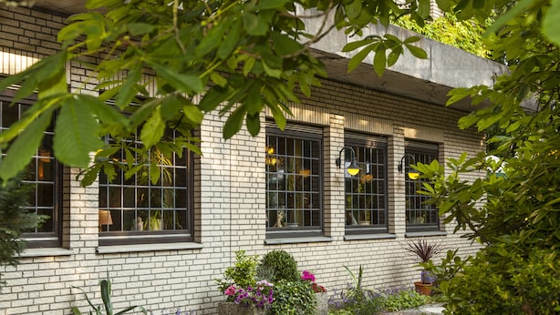 Un bâtiment en briques doté de grandes fenêtres et d’un jardin où poussent différentes plantes et fleurs.