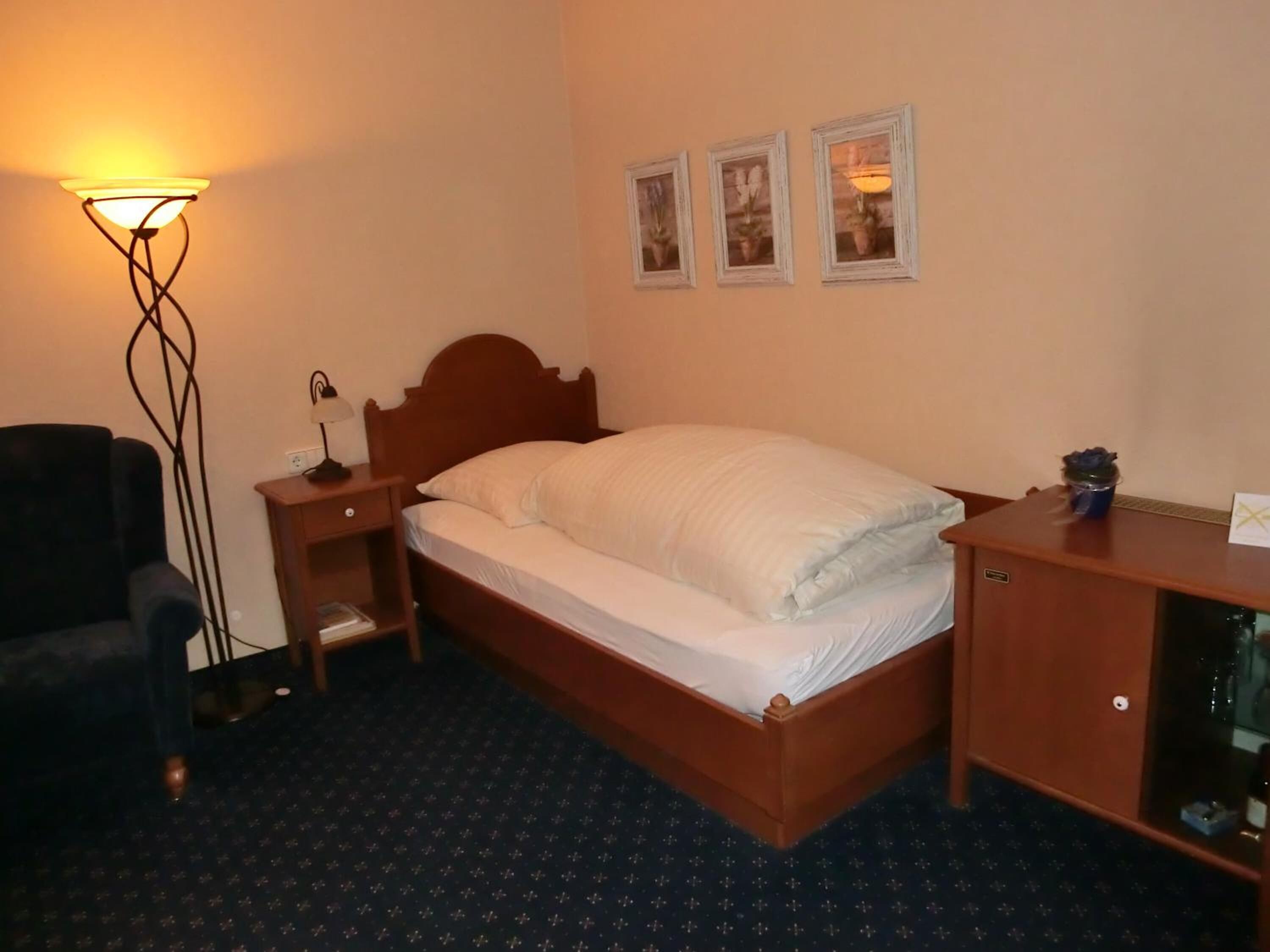 Een hotelkamer met een bed, nachtkastje, lamp, stoel en bureau met spiegel.