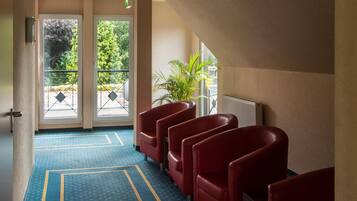Un hall d’hôtel avec un tapis bleu, des fauteuils rouges et une vue sur la verdure grâce à de grandes fenêtres.
