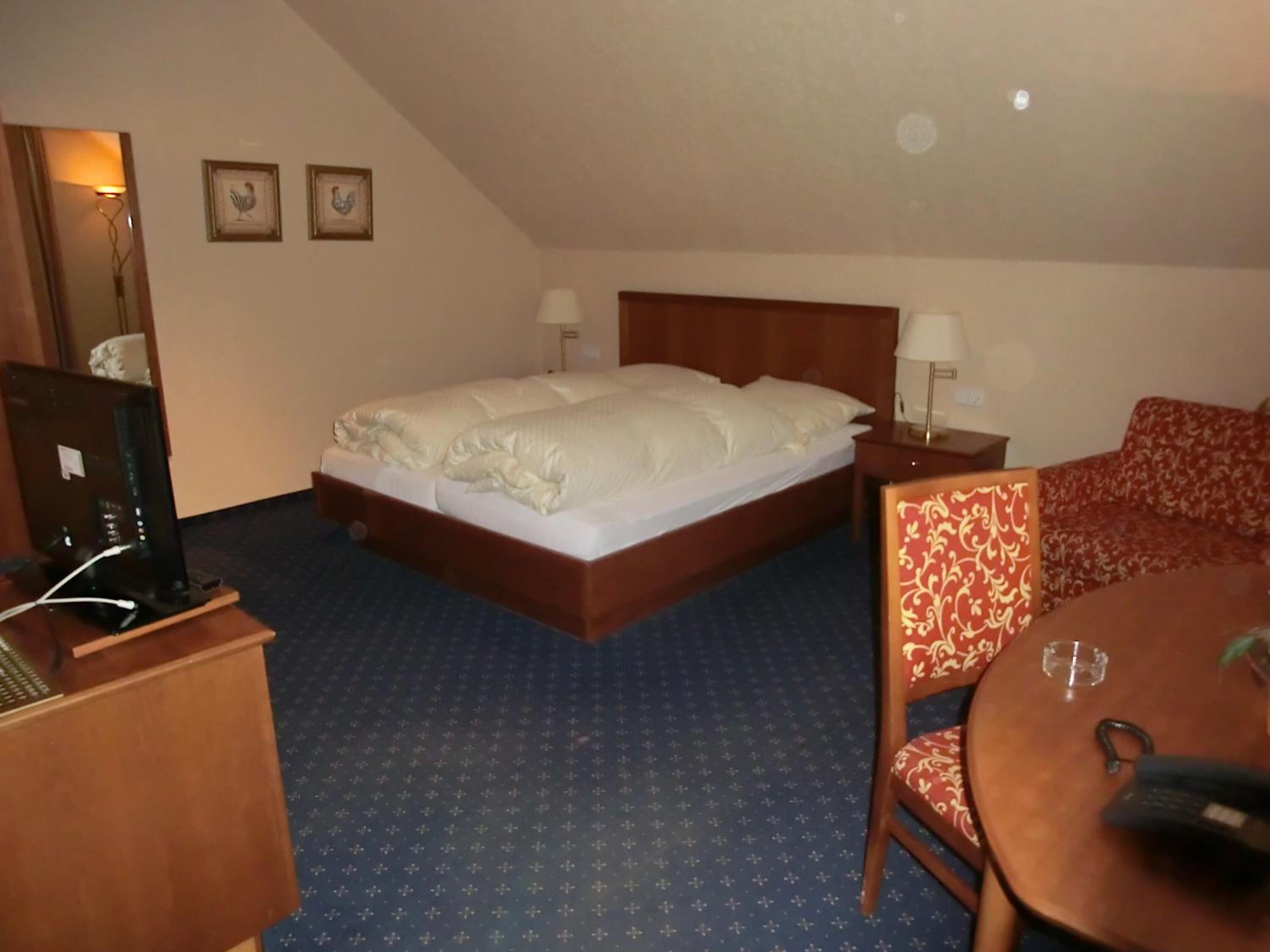 Hotelkamer met een groot bed, een bureau met een computer, een stoel, een klein tafeltje met een glas, en twee wandlampen.
