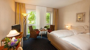 Une chambre d’hôtel avec un lit, un bureau avec une lampe, une chaise, une télévision et une fenêtre avec des rideaux.