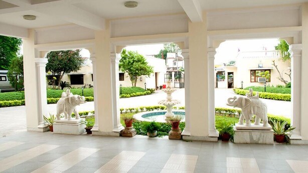 Una entrada cubierta con dos estatuas de elefantes, una fuente y un jardín bien cuidado visible a través de los arcos.