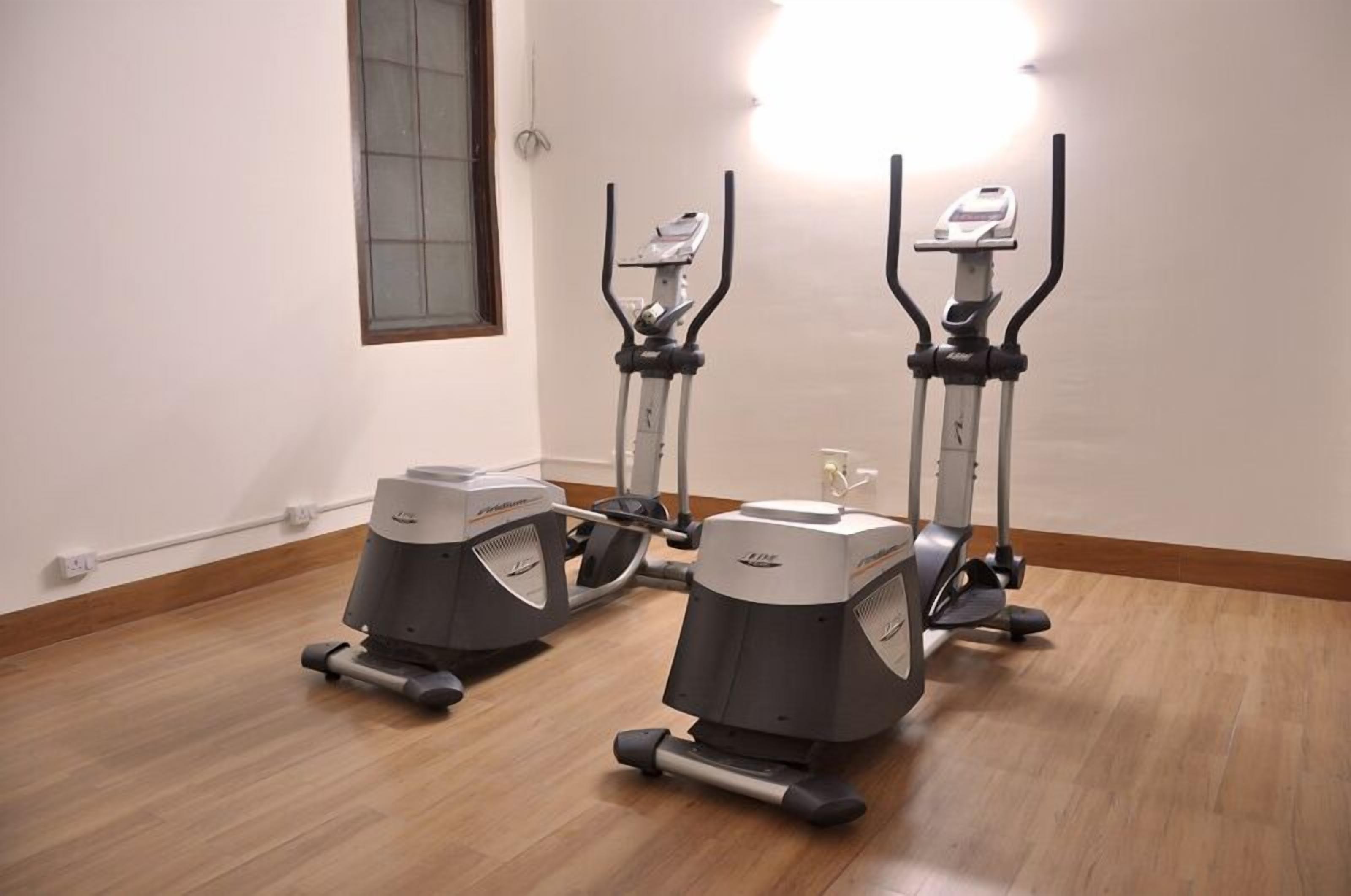 Two stationary bikes in a room with wooden flooring and white walls.