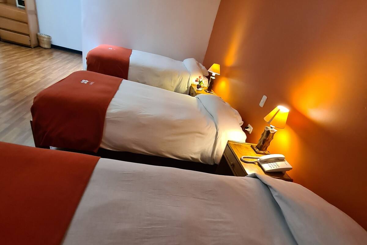 Ett hotellrum med två sängar, var och en med ett rött och vitt sängöverkast, ett nattduksbord med en lampa och en liten prydnadsföremål.
