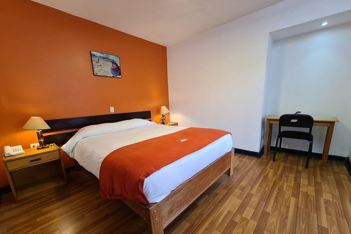 Ett hotellrum med en s äng i trä, två sänglampor, ett skrivbord och en stol.