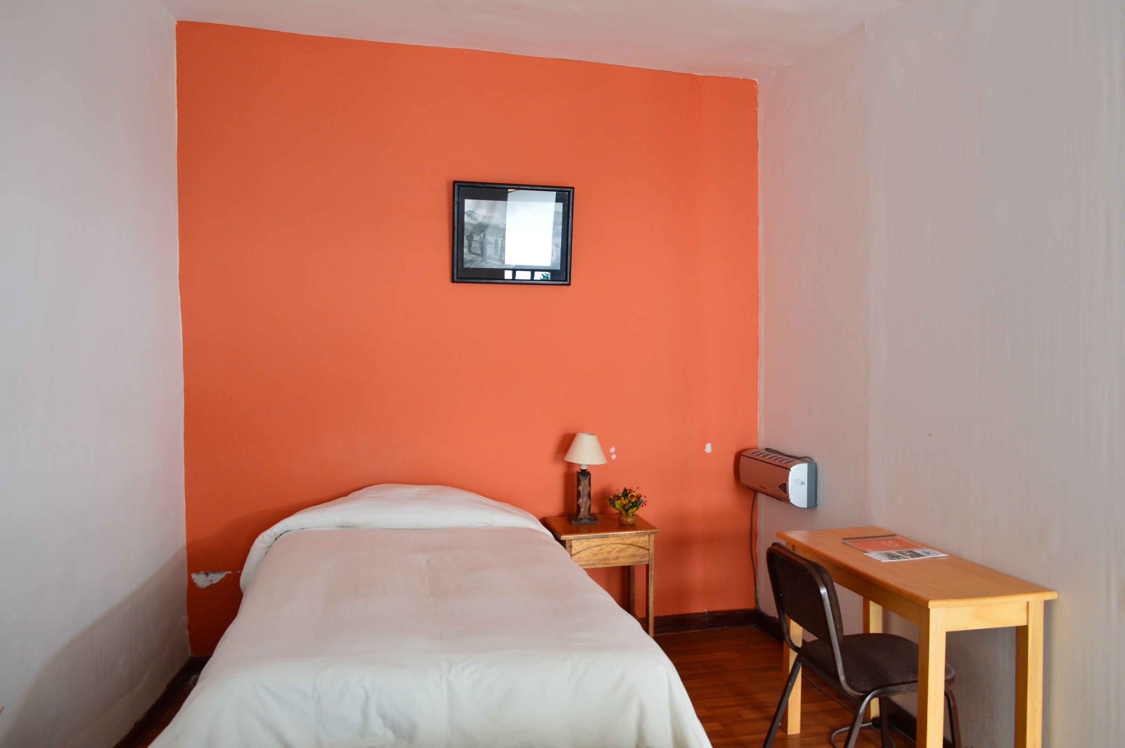 A room with a bed, a desk, a chair, a lamp, and a picture frame on the wall.