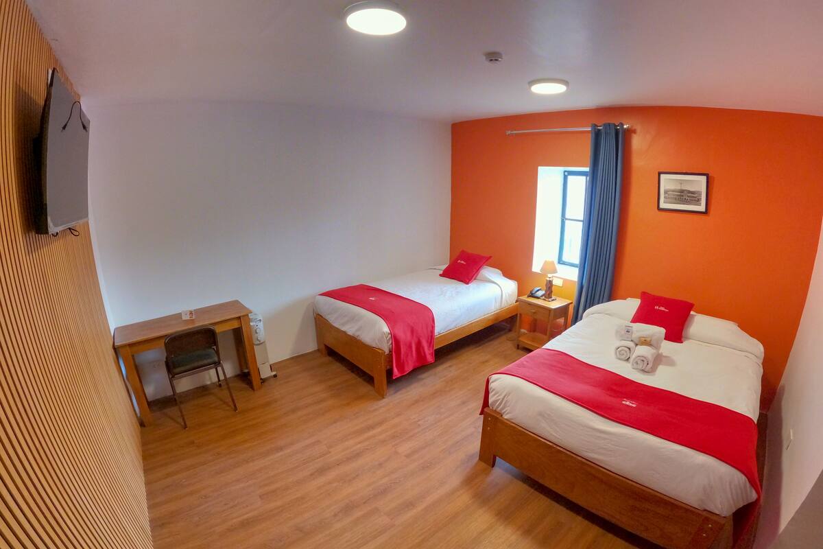Ett hotellrum med två sängar, ett skrivbord och ett fönster med gardiner.