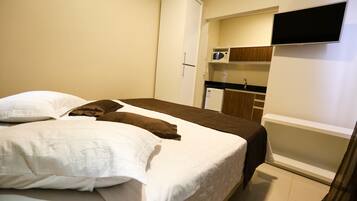 Een slaapkamer met een bed, kussens, een kledingkast, een televisie en een kitchenette.