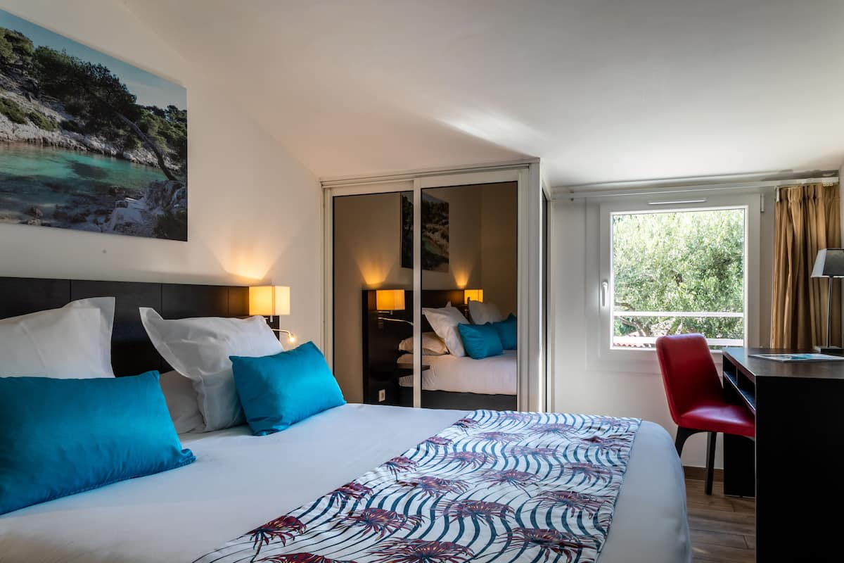 Una habitación de hotel con cama, escritorio, silla y un amplio ventanal.
